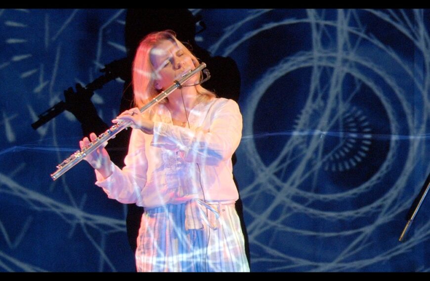 Ewelina Serafin gra na flecie. W tle widać niebieskie wizualizacje.