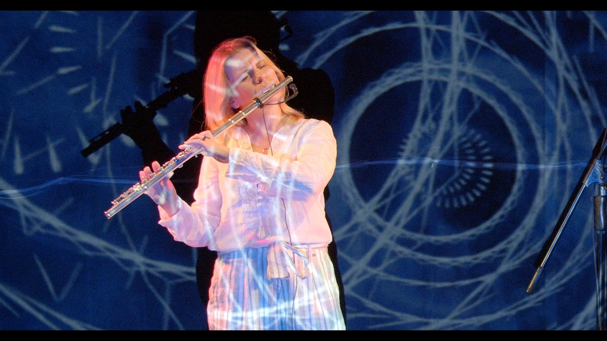 Ewelina Serafin gra na flecie. W tle widać niebieskie wizualizacje.