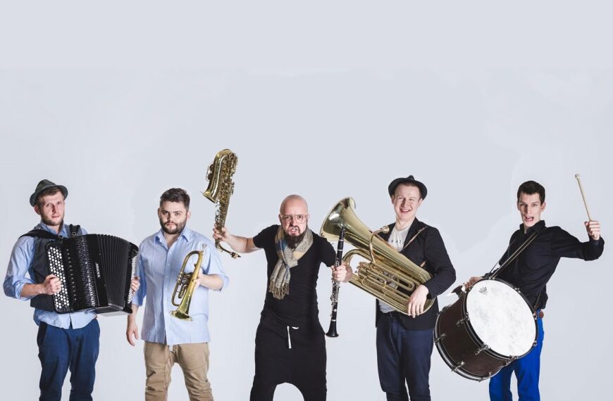 Pięcioro muzyków z Bum Bum Orkestar na białym tle trzyma w rękach instrumenty. Od lewej: akordeon, trąbka, saksofon i flet, tuba, werbel.