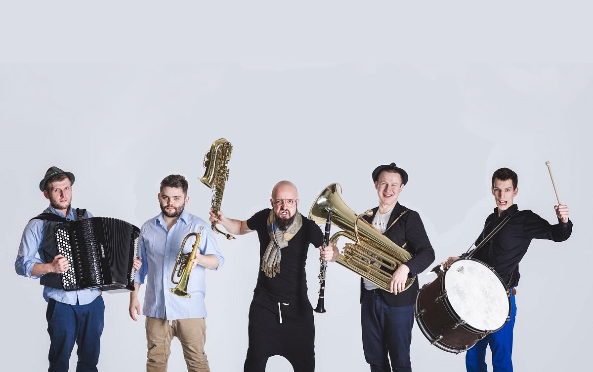 Pięcioro muzyków z Bum Bum Orkestar na białym tle trzyma w rękach instrumenty. Od lewej: akordeon, trąbka, saksofon i flet, tuba, werbel.