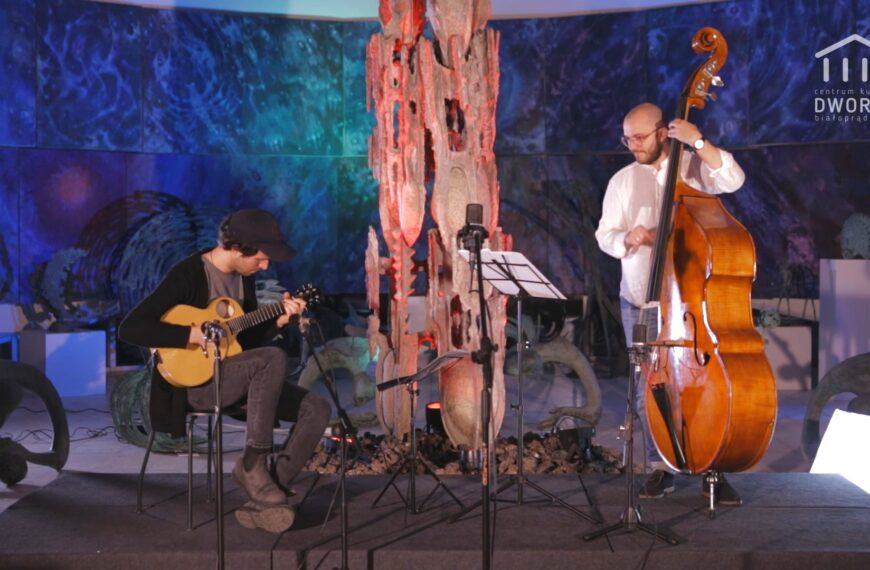 Na scenie Szymon Mika i Piotr Południak. Po lewej siedzący na krześle męczyzna gra na gitarze, po prawej meżczyzna gra na kontrabasie.