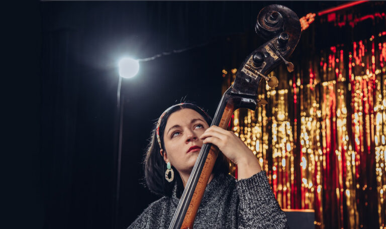 Kamila Drabek gra na kontrabasie. W tle reflektor i słota scenografia.