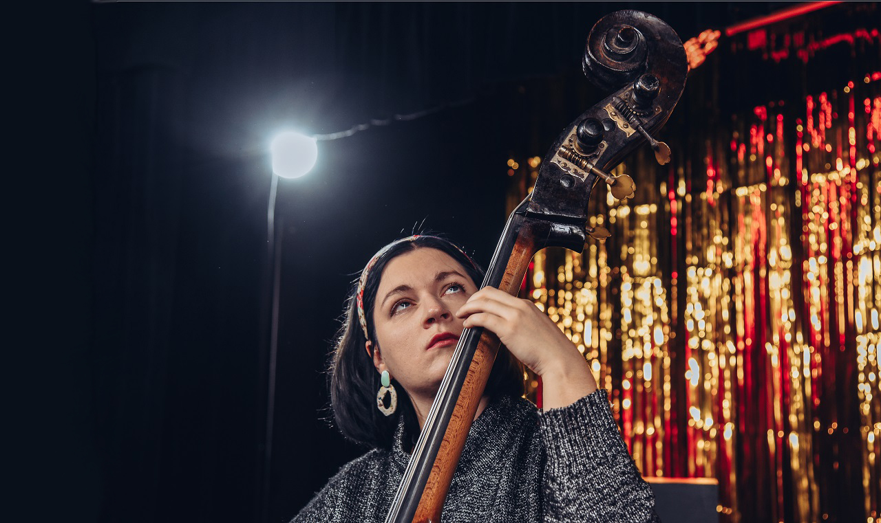Kamila Drabek gra na kontrabasie. W tle reflektor i słota scenografia.