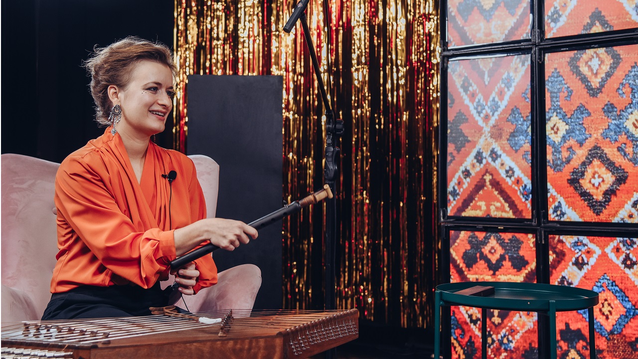 Uśmiechnięta Zofia Trystuła-Hovhannisyan siedzi na fotelu, w ręku trzyma instrument duduk.