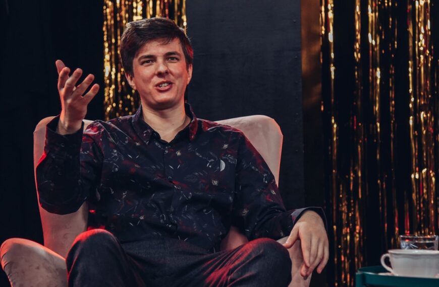 Mateusz Pałka siedzi na fotelu. Gestykuluję ręką.