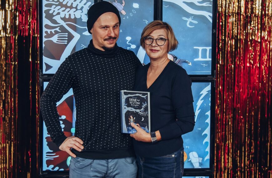 Mikołaj Rejs i kobieta stoją obok siebie. Patrzą w obiektyw, Kobieta trzyma w rękach książkę.