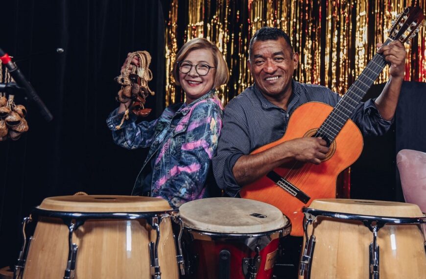 Na pierwszym planie bębny. Za nimi siedzą Tomas Celis Sanchez i kobieta.