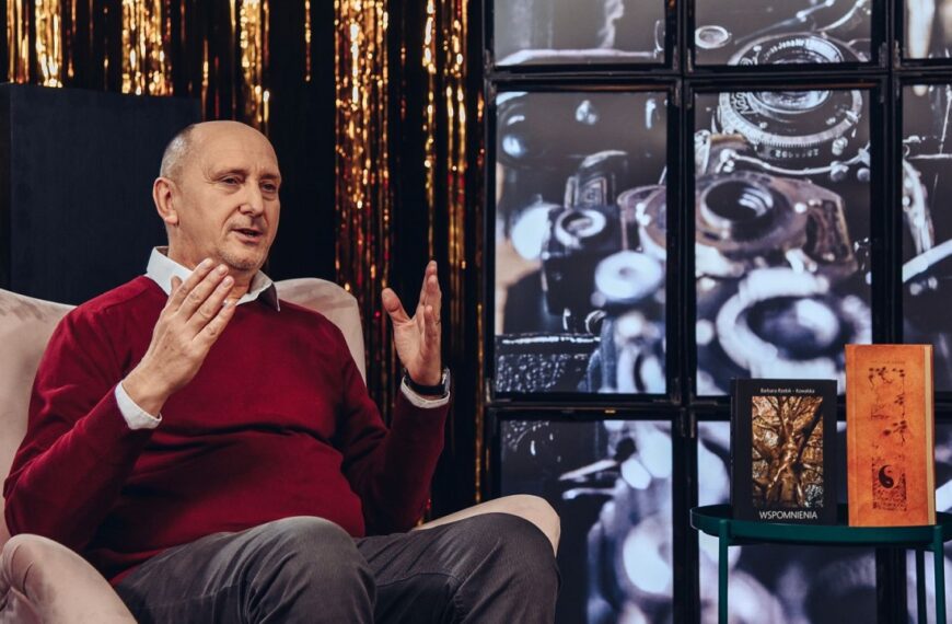 Andrzej Wodziński siedzący na fotelu tłumaczy coś gestykulując rękami. Obok na stoliku książki.