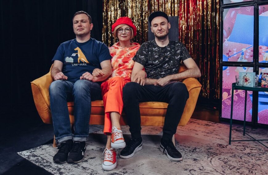 Na kanapie z powaznymi minami siedzi dwóch mężczyzn i w środku kobieta.