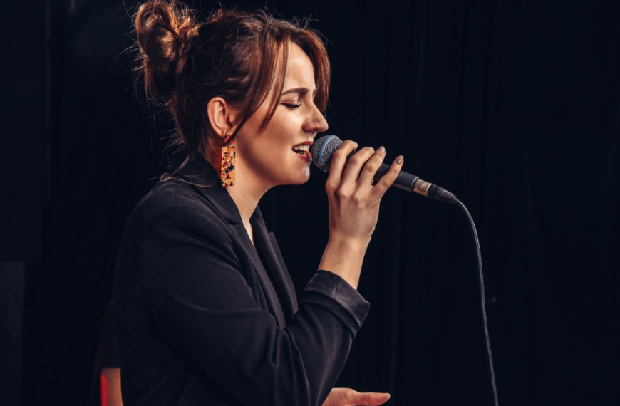 Basia Dratwińska odwrócona bokiem śpiewa do mikrofonu.