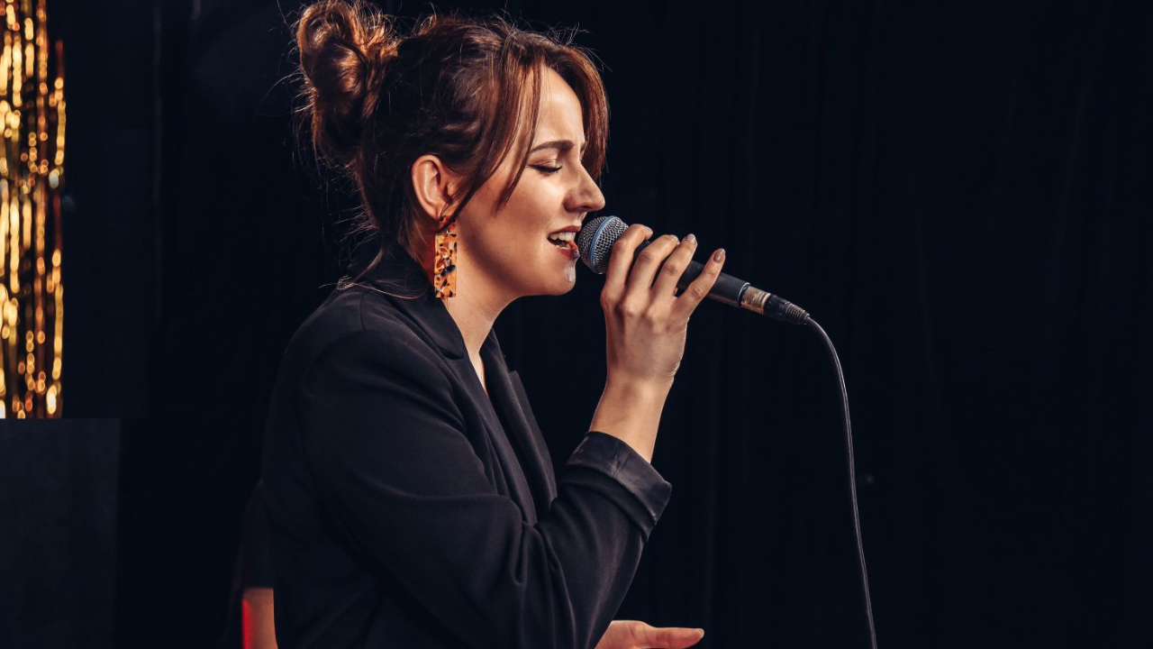 Basia Dratwińska odwrócona bokiem śpiewa do mikrofonu.