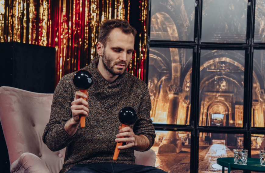 Jakub Frączek siedząc na rożowym fotelu gra na marakasach