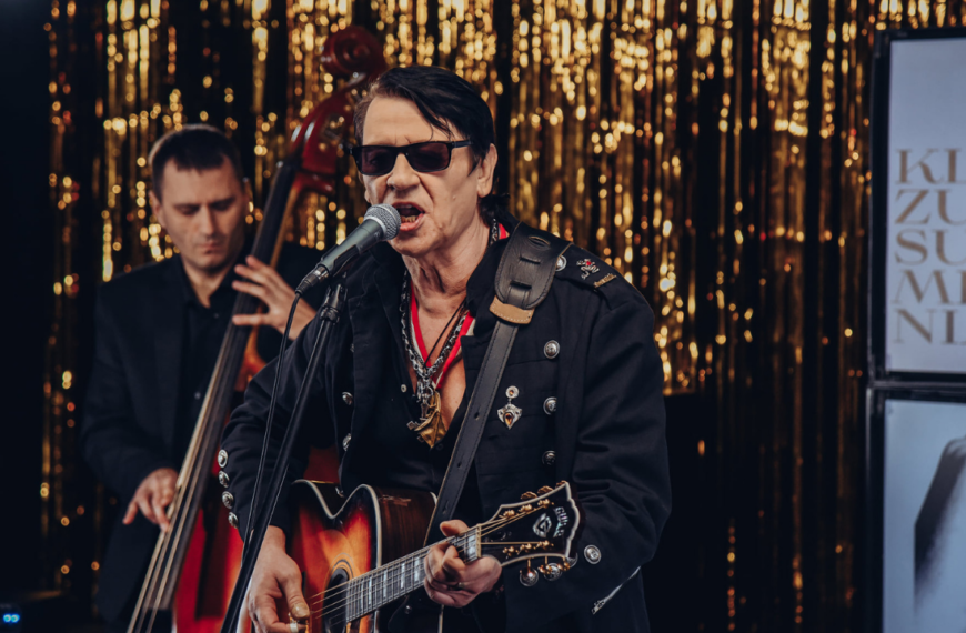 Maciej Maleńczuk w ciemnych okularach gra na gitarze i śpiewa