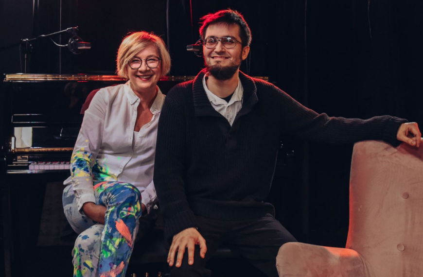 Kobieta i Kuba Płużek pozują uśmiechnięci do zdjęcia. W tle fortepian.