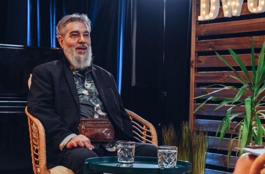 Jorgos Skolias siedzi na wiklinowym krześle. W tle studio nagraniowe.