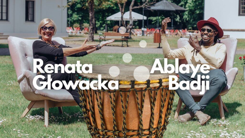 Renata Głowacka i Ablaye Badji siedzą na fotelach na trawie przed Dworkiem Białoprądnickim a między nimi stoki duży afrykanski bęben.